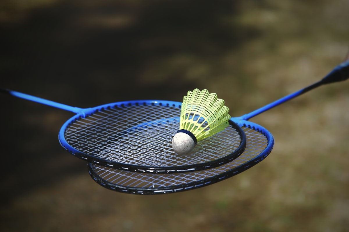 Two badminton rackets crossed outdoors with a yellow shuttlecock resting on the strings