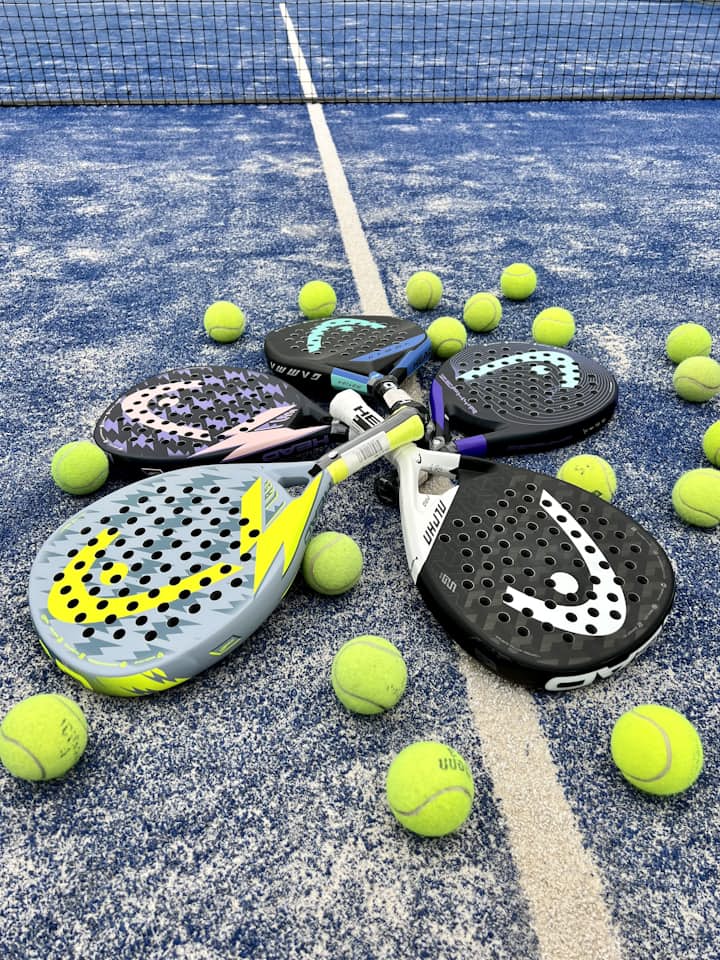 Several padel rackets fanned out with balls on a blue court — the range of paddles a beginner has to choose between.
