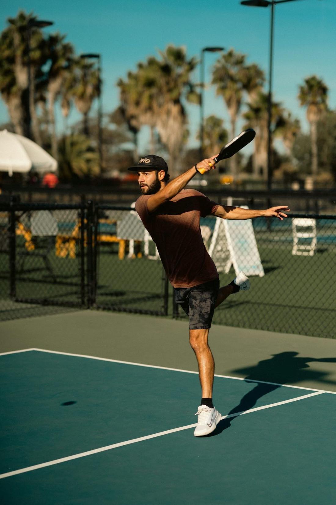 Solo player swinging a paddle on a tennis court — the kind of solo-drill scenario a ball machine enables