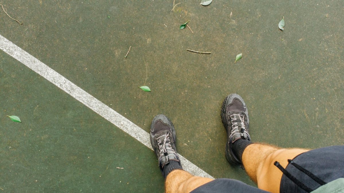 Pies de un jugador plantados sobre una superficie de sport court verde, en plena posición sobre la línea de banda pintada