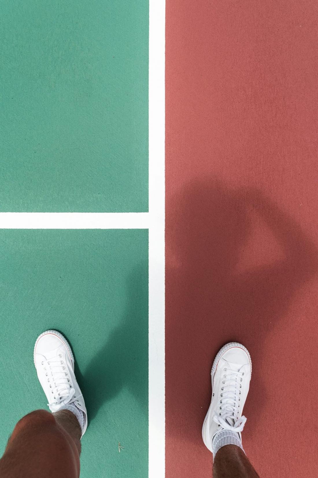 Zapatillas de pista blancas sobre la línea que separa la superficie verde y la roja pintadas de una pista de tenis de exterior