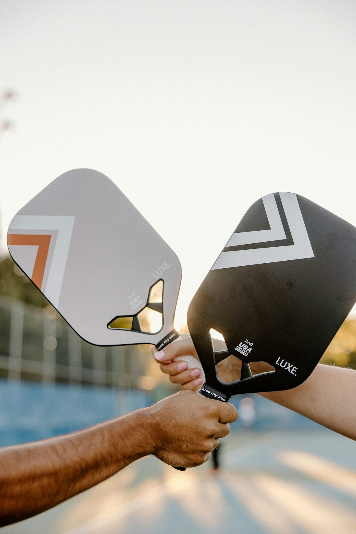 Dos jugadores de pickleball sosteniendo sus palas en una pista al aire libre, listos para jugar
