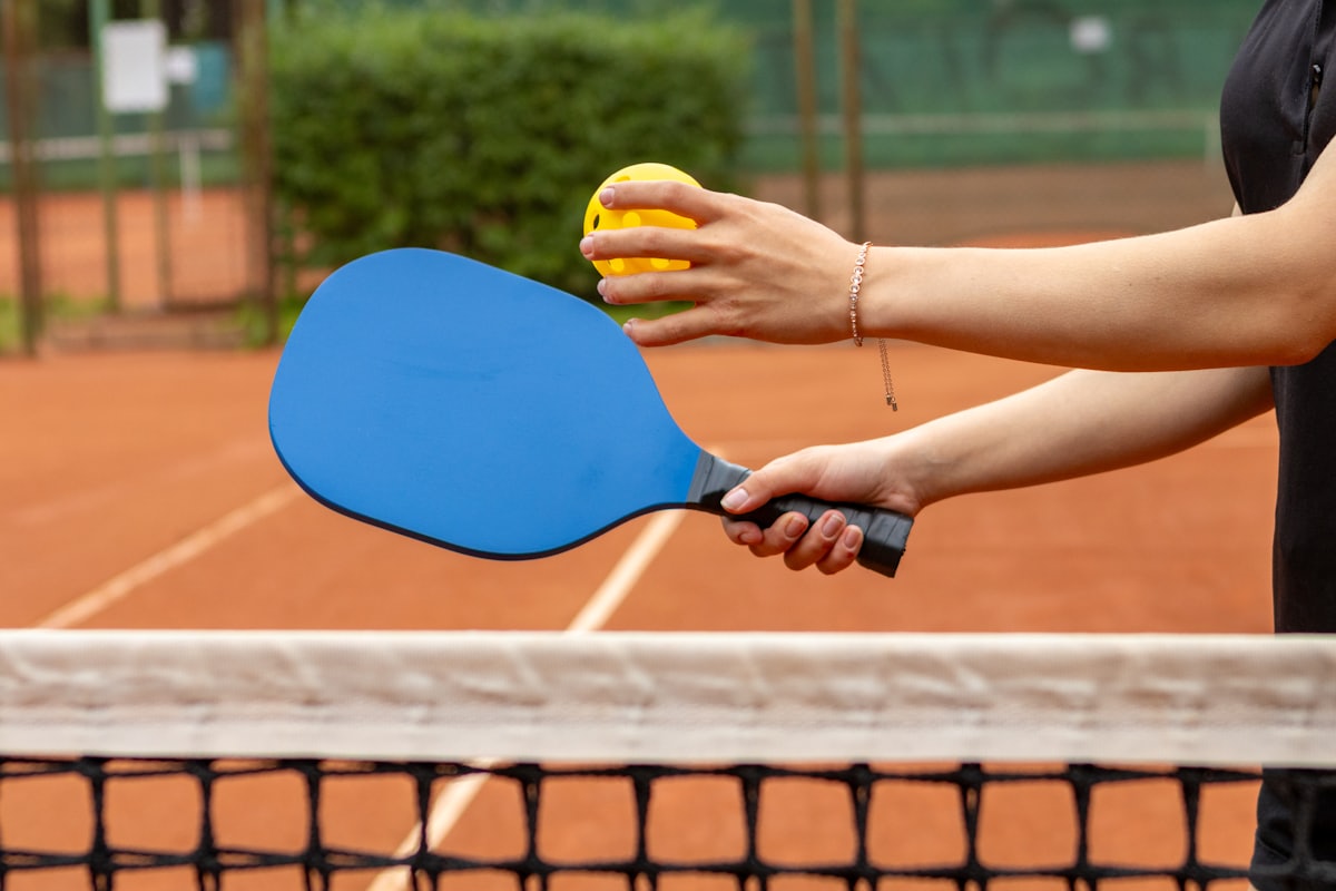 A player holding a pickleball paddle and ball together at the net, preparing to play