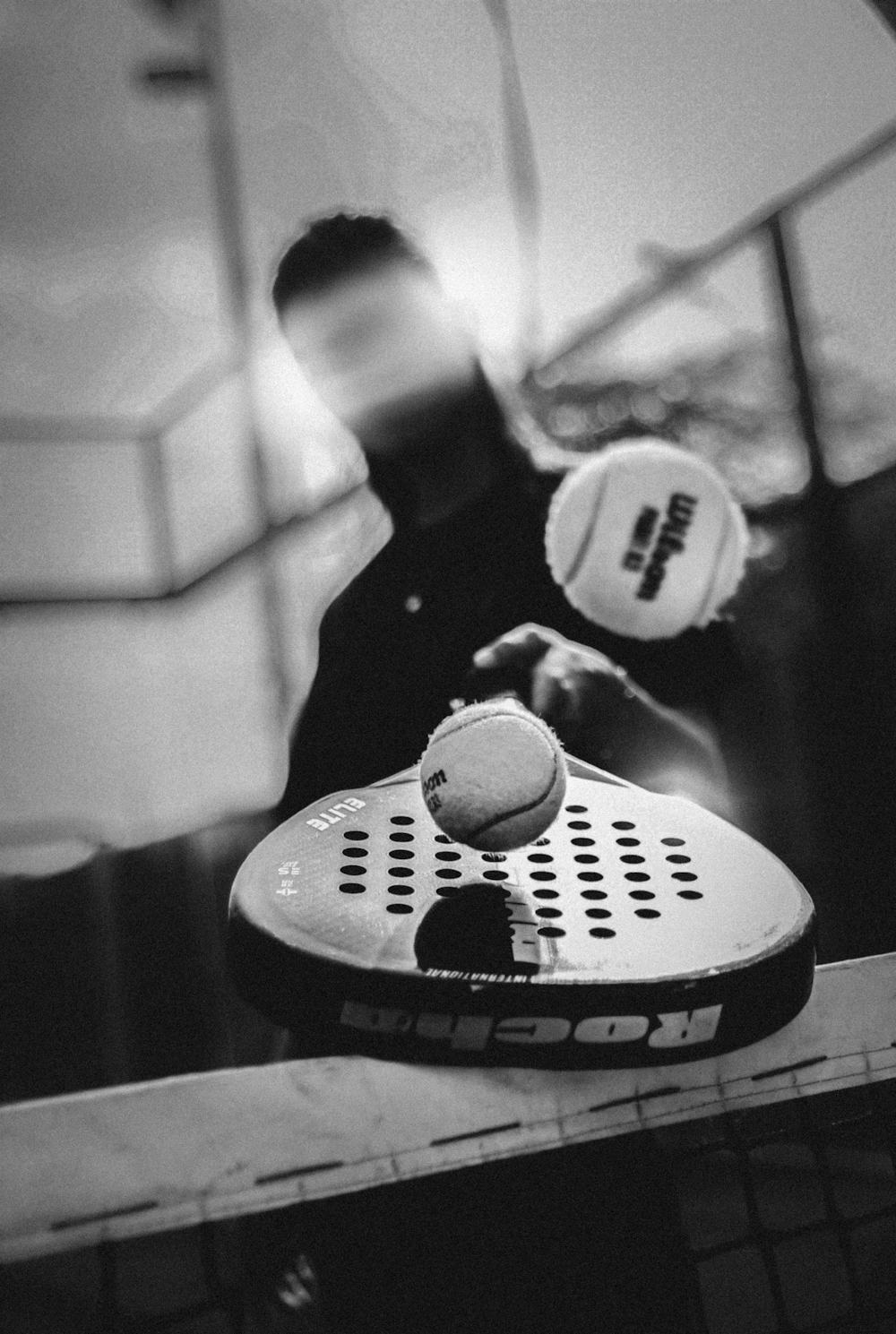 Close-up of a padel player's underhand serve motion, ball and paddle meeting just above the net in a black-and-white action shot.