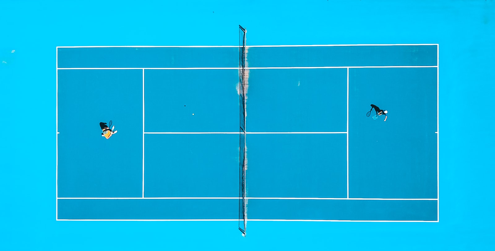 Vista aérea de dos jugadores en una pista de deporte de raqueta, la geometría compartida que conecta pickleball, tenis y pádel
