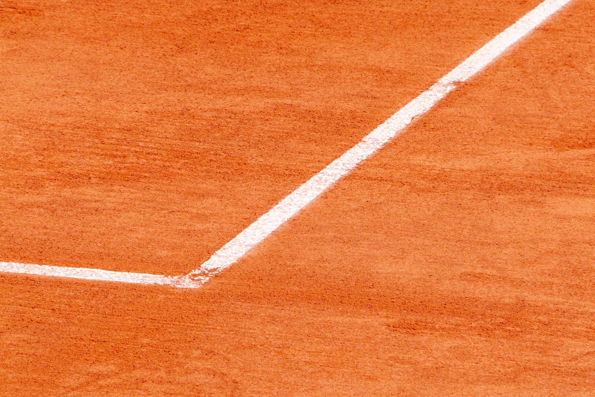 Close-up of a tennis court's white baseline and sideline meeting at a corner on red clay, the kind of line a ball's landing spot gets judged against