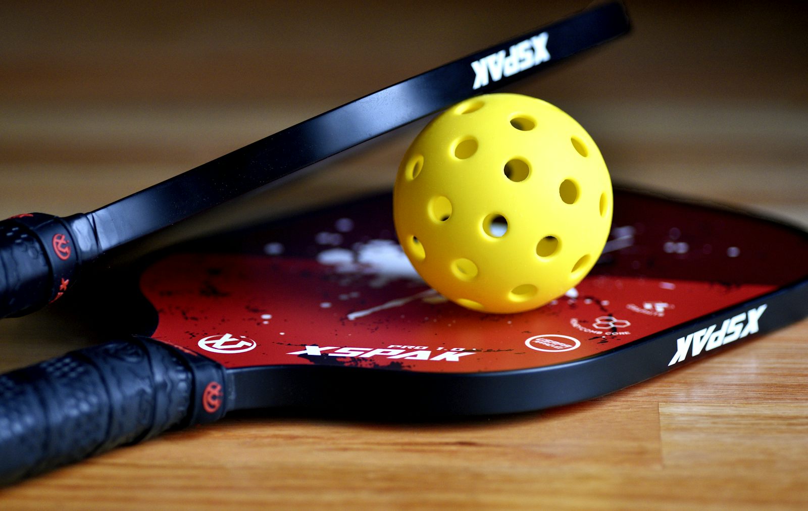 Una bola de pickleball apoyada sobre la cara desgastada de una pala — el tipo de desgaste que indica que toca cambiarla